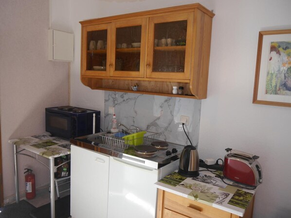 Une cuisine compacte équipée d’un four à micro-ondes, d’une bouilloire, d’un grille-pain et d’un placard au-dessus de l’évier.