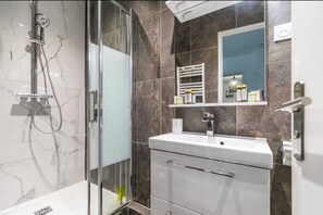 A modern bathroom with a glass shower enclosure, a white sink, and a marble-tiled wall. - Charming appt - 1BR/4P - Montreuil - Proche Paris (Montreuil)