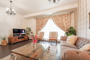 A living room with a television, two armchairs, a sofa, a glass coffee table, and a chandelier. - Spacious 3BR in Amwaj | Steps from the Beach (Dubai)