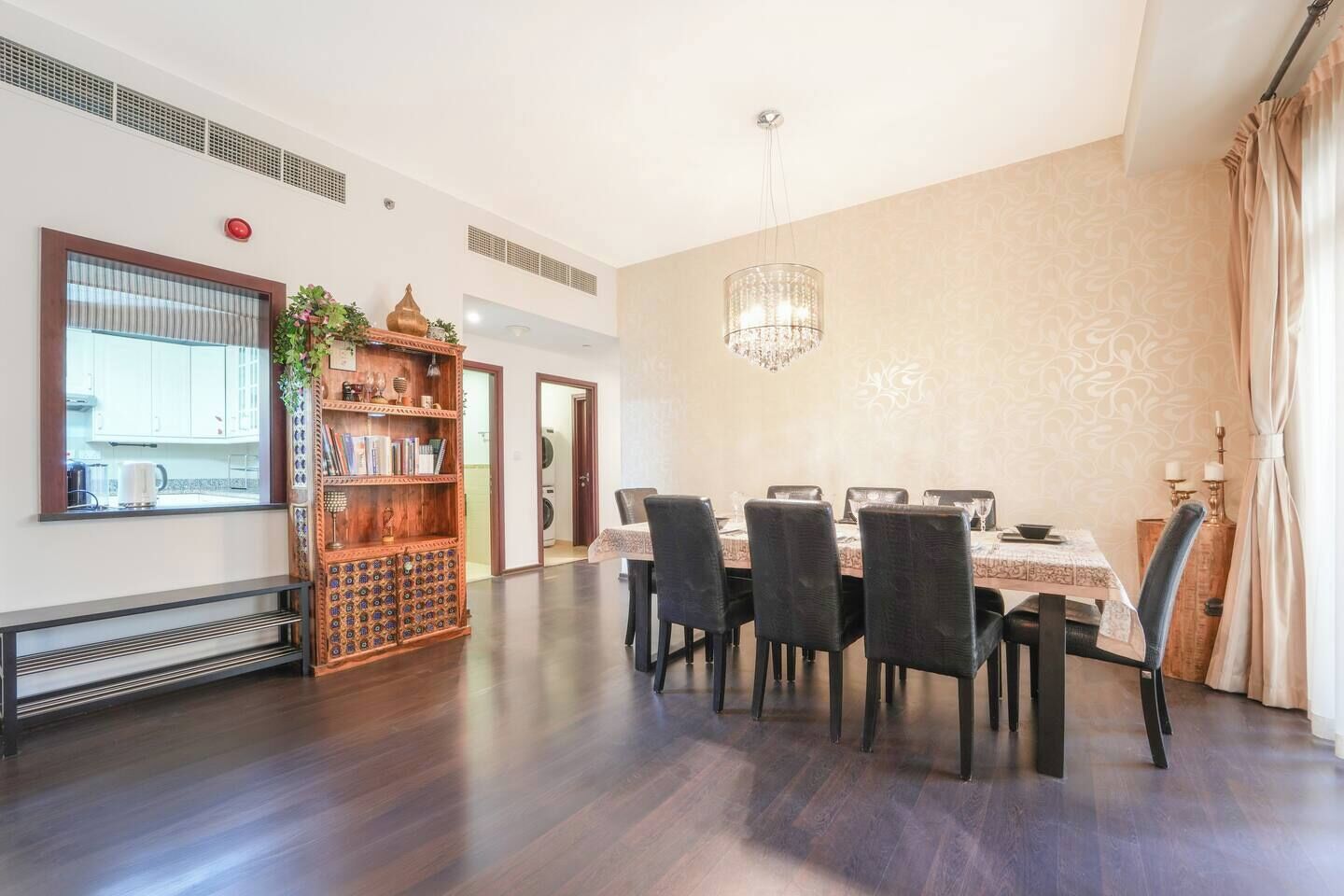 Een eetgedeelte met een tafel voor vier personen, een kroonluchter en een boekenplank.