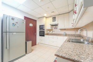 A kitchen with a stainless steel refrigerator, a microwave, an oven, and a granite countertop. - Spacious 3BR in Amwaj | Steps from the Beach (Dubai)