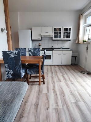 A modern kitchen with white cabinets, a wooden dining table, and chairs with a leaf pattern. - Cozy Holiday Apartment with Private Garden (Milmersdorf)