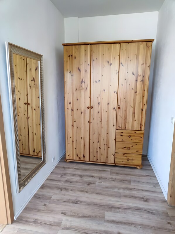A room with a wooden wardrobe, a mirror, and a wooden floor.