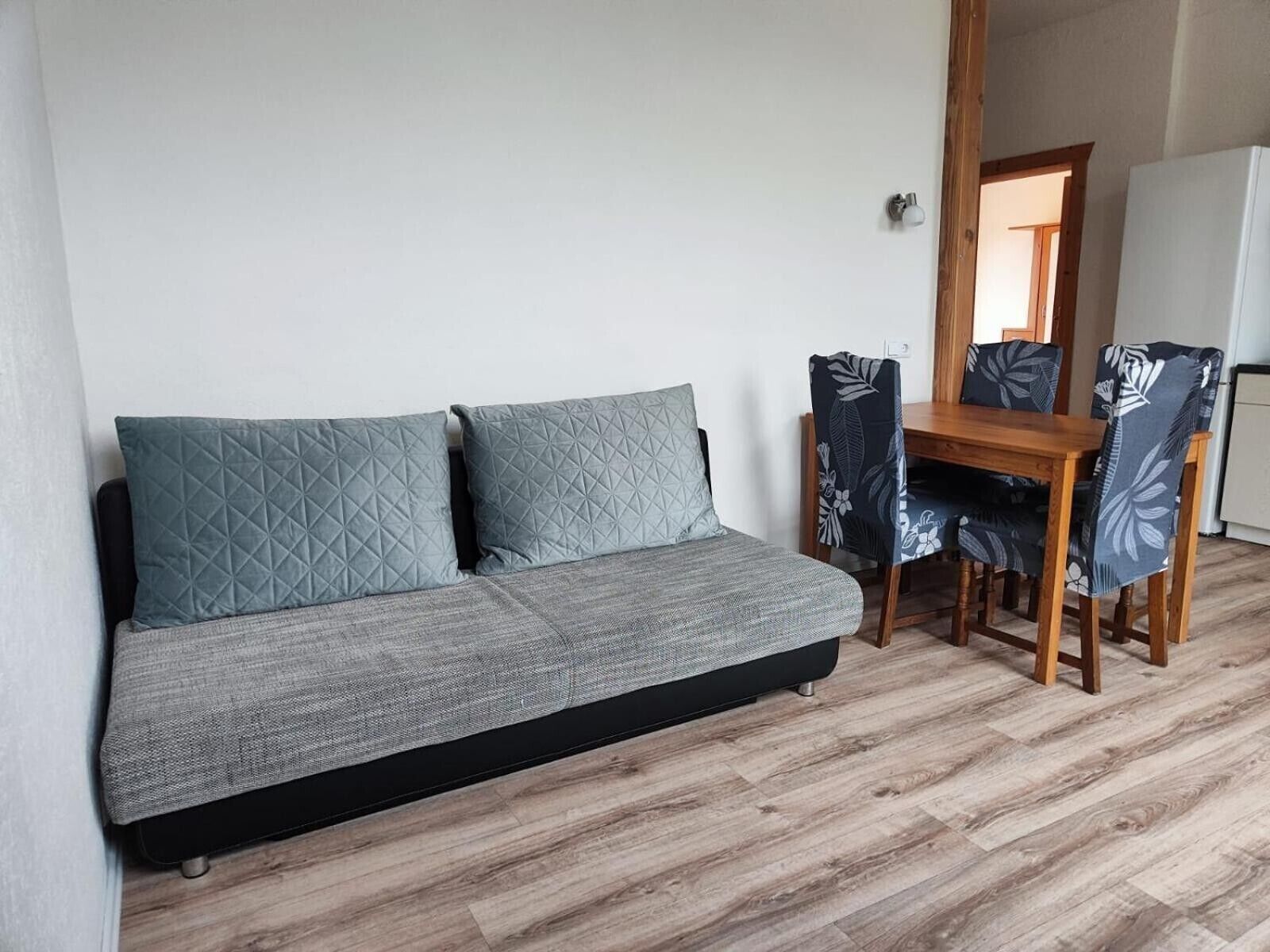 A sofa with two pillows, a wooden dining table, and chairs with a leaf pattern.