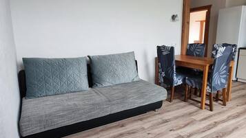 A sofa with two pillows, a wooden dining table, and chairs with a leaf pattern.