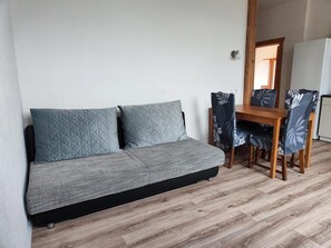 A sofa with two pillows, a wooden dining table, and chairs with a leaf pattern.