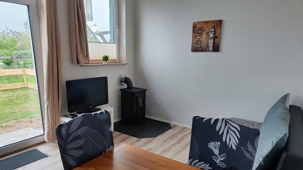Um quarto com uma mesa de madeira, um sofá com almofadas estampadas, uma televisão, um pequeno aquecedor preto e uma janela com cortinas.