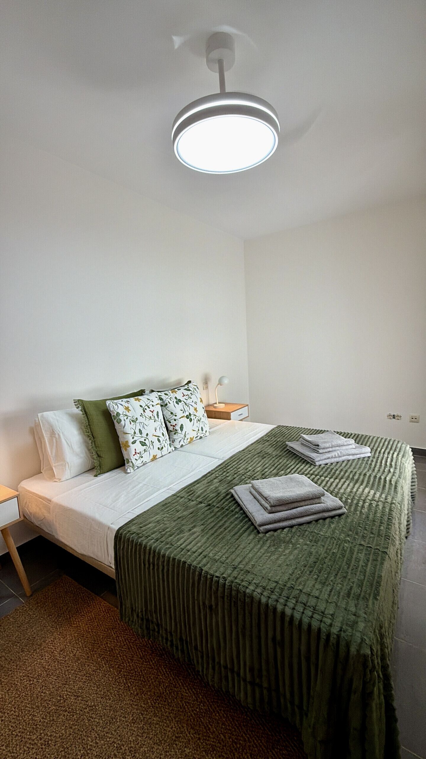 A neatly arranged bedroom with a bed, pillows, a bedside table, and a lamp.