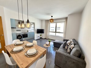 Un espacio habitable moderno con comedor, un sofá gris y una cocina equipada con lavadora.