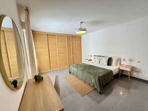 A bedroom with a bed, bedside tables, a desk, a mirror, and a ceiling fan. - Dragos Suites 201 (Arrecife)