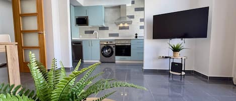 Una cocina moderna con lavadora, un televisor de pantalla plana montado en la pared y un helecho grande en primer plano.