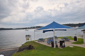 A lakeside pavilion with picnic tables and a grill, overlooking a calm lake. - In the Middle of it All -2 Pools,Grill,Fishing,Boat Launch,Boat rental next door (Osage Beach)