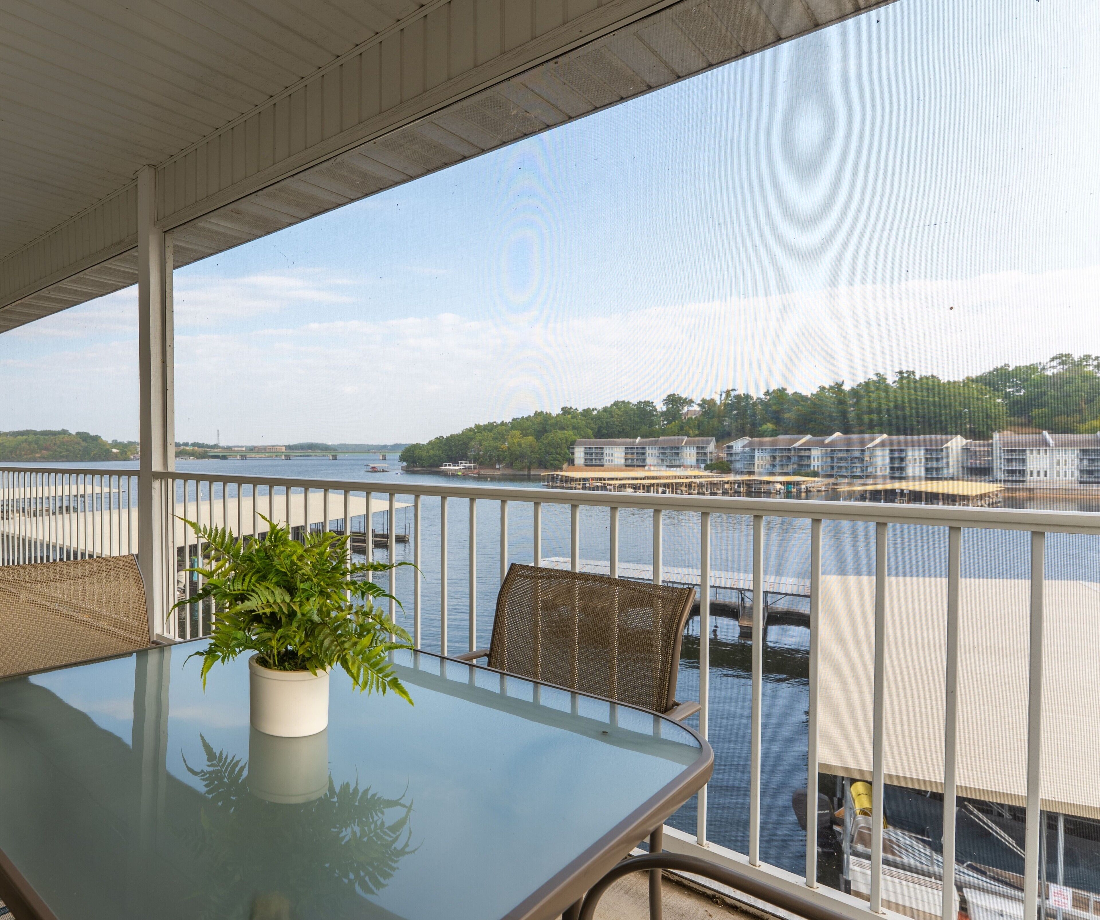 Ein Balkon mit einem Glastisch und Stühlen, mit Blick auf einen Wasserweg mit Gebäuden und einer Brücke.