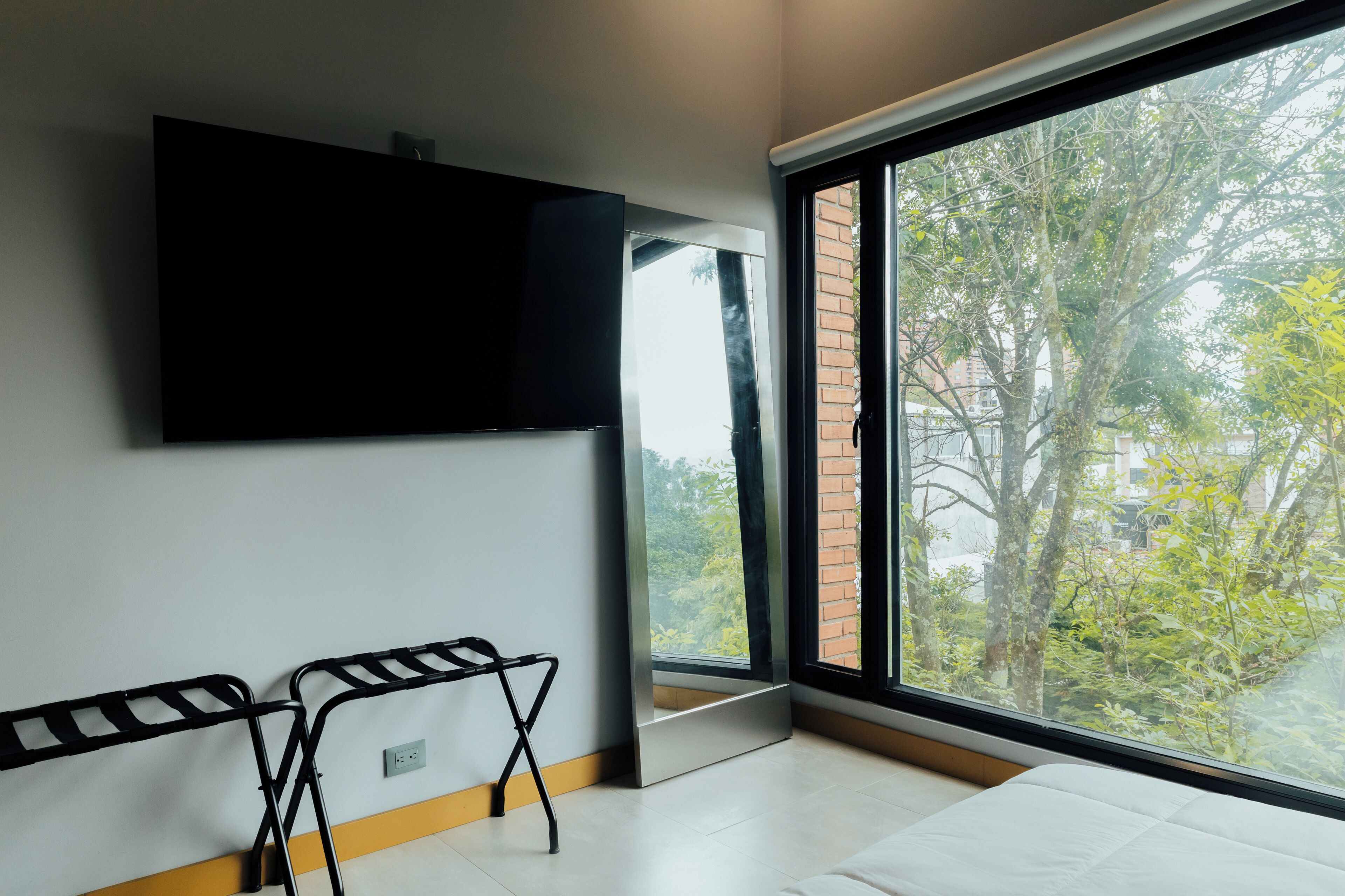 A modern room with a large window, a flat-screen TV mounted on the wall, and a foldable chair.
