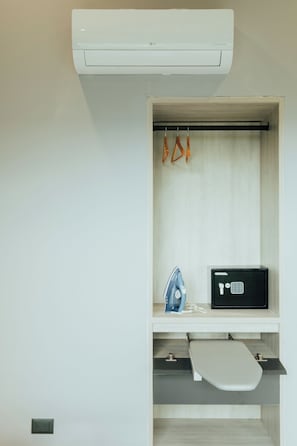 Eine weiße Wand mit integrierter Klimaanlage, einem schwarzen Sicherheitspanel und einem kleinen Bügelbrett.
