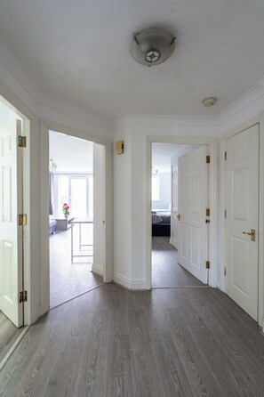 A hallway with white walls, a ceiling light, and a door leading to a room with a bed. - Karazo Ltd - 2 bedroom home in Croydon (Croydon)