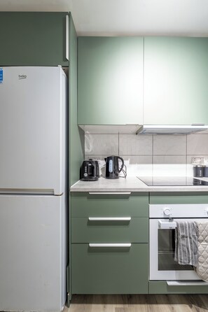 A kitchen with green cabinets, a white refrigerator, a kettle, and a toaster on the counter. - Karazo Ltd - 2 bedroom home in Croydon (Croydon)