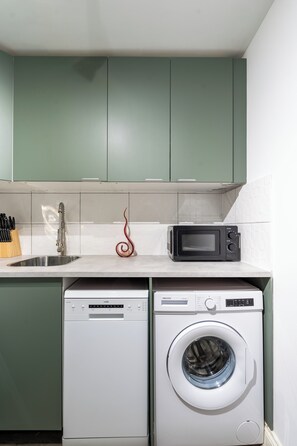 A compact kitchen with a dishwasher, a washing machine, and a microwave. - Karazo Ltd - 2 bedroom home in Croydon (Croydon)