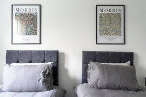 Two beds with grey headboards and pillows, each with a framed quote by William Morris on the wall above. - Karazo Ltd - 2 bedroom home in Croydon (Croydon)