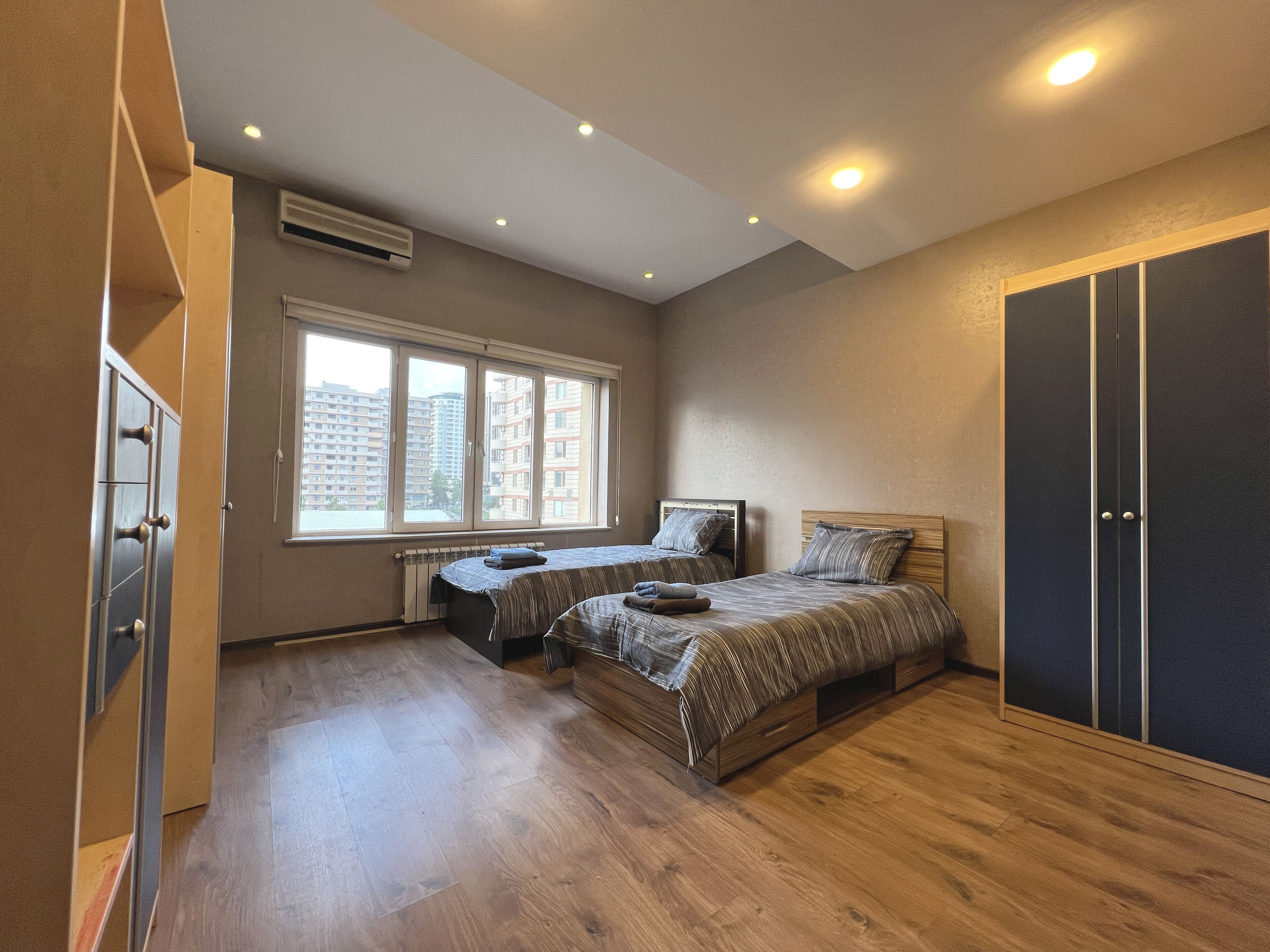 Ein Schlafzimmer mit zwei Betten, einem Kleiderschrank und einem Fenster mit Blick auf Gebäude.