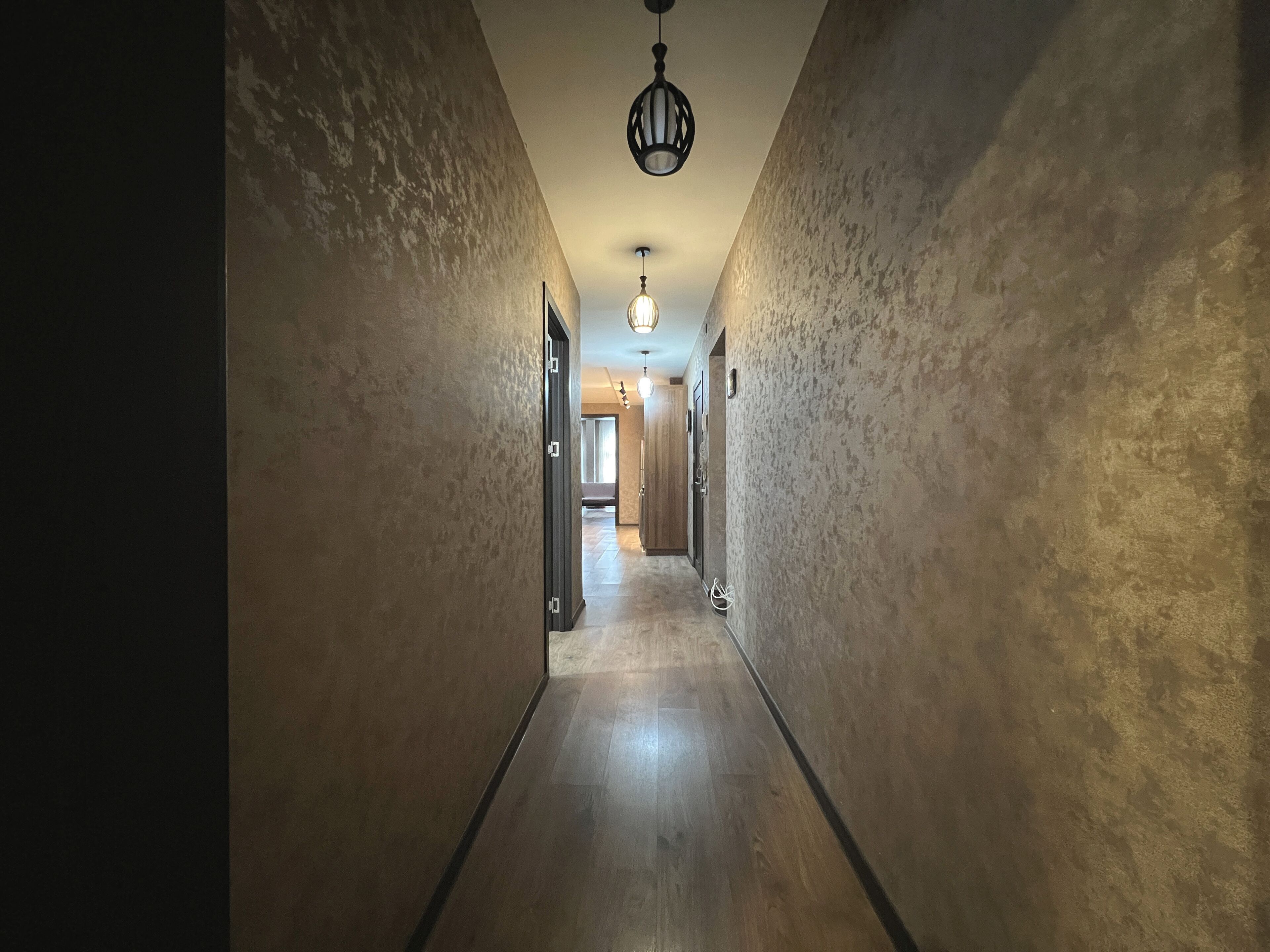 Un pasillo con paredes con textura y suelo de madera, que conduce a una habitación con una puerta al final.