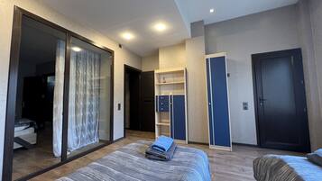 Een moderne hotelkamer met een groot bed, een kledingkast, een bureau en een schuifdeur naar een balkon.