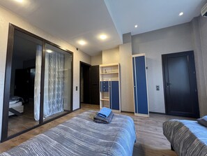 A modern hotel room with a large bed, a wardrobe, a desk, and a sliding door leading to a balcony. - Spacious 2BR near Winter Park - Sleeps 5 (Baku)