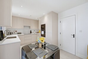 A modern kitchen with a dining area, featuring a built-in oven, a coffee machine, and a sink. - 2-Bed with Balcony in Northfields -Apt 4 (London)
