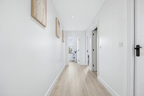 A hallway with white walls, wooden flooring, and doors leading to other rooms. - 2-Bed with Balcony in Northfields -Apt 4 (London)