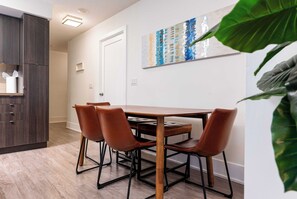 A dining area with a wooden table and four brown chairs, a dark wooden cabinet, and a large abstract painting on the wall. - Modern 3BR Retreat, Bright & City-View (Toronto)