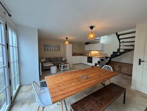 A modern kitchen with a dining area, a staircase, and a large window. - Vrbo Property (Saint-Vaast-la-Hougue)