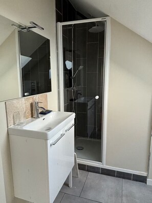 Ein Badezimmer mit weißem Waschtisch, einem Spiegel und einer Duschkabine.
