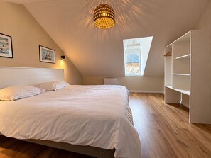 A bedroom with a large bed, a skylight, a hanging light fixture, and built-in shelving. - Vrbo Property (Saint-Vaast-la-Hougue)