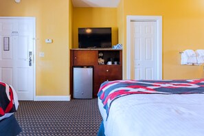 Una habitación de hotel con cama, televisión, un refrigerador pequeño y un armario de madera.