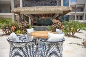 An outdoor seating area with a round wooden table and wicker chairs, surrounded by decorative plants and a patterned wall. - New Luxury Condo Near Eagle Beach - Pool & Gym - Walishali Condo (Oranjestad)