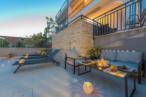 An outdoor patio with a stone wall, a sofa, a table with candles, and lounge chairs. - Villa Seaview with heated pool-Apartment Luxury (Split)