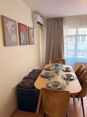 A dining area with a table set for four, a bench, and a window with curtains. - Light and spacious flat in central Istanbul (Şişli)