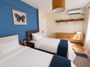 A hotel room with two beds, a bedside table with a lamp, a wardrobe, a hanging clothes rack, and an air conditioning unit. - Light and spacious flat in central Istanbul (Şişli)