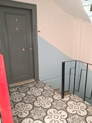 A staircase with a patterned floor, a grey door with a lock, and a red object on the left. - Light and spacious flat in central Istanbul (Şişli)
