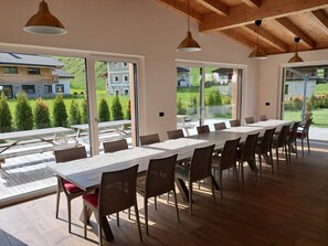 A spacious dining area with a long table and chairs, large windows, and a view of a green landscape.