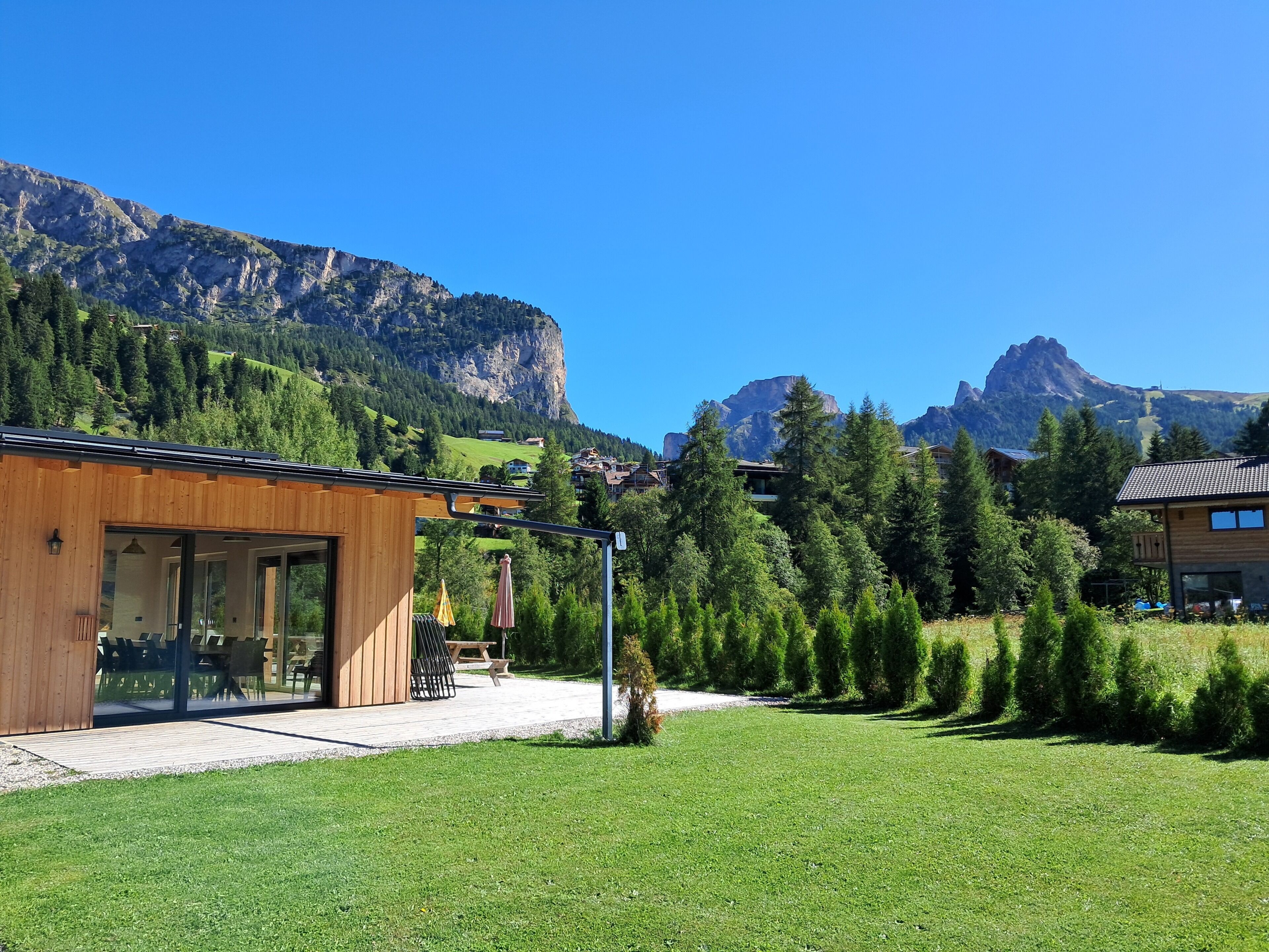 Ein modernes Holzgebäude mit einer Terrassenfläche, umgeben von üppiger Vegetation und Bergen im Hintergrund.