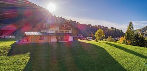 A two-story house with a large front yard, a wooden deck, and a mountain backdrop.