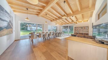 Une cuisine spacieuse avec des poutres en bois, de grandes fenêtres et un coin repas doté de chaises en osier.