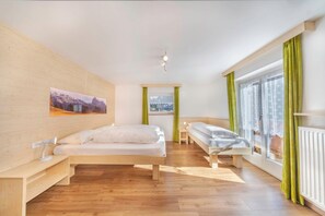 A modern bedroom with a wooden floor, a bed, a bench, a window with curtains, and a painting on the wall.
