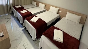 Habitación de hotel con cuatro camas dispuestas en fila, cada una con cubrecama blanco y manta roja.