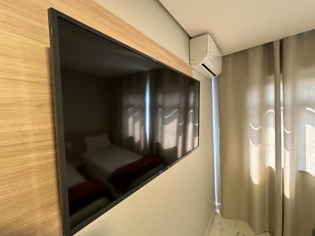A wall-mounted television in a room with a bed and curtains.