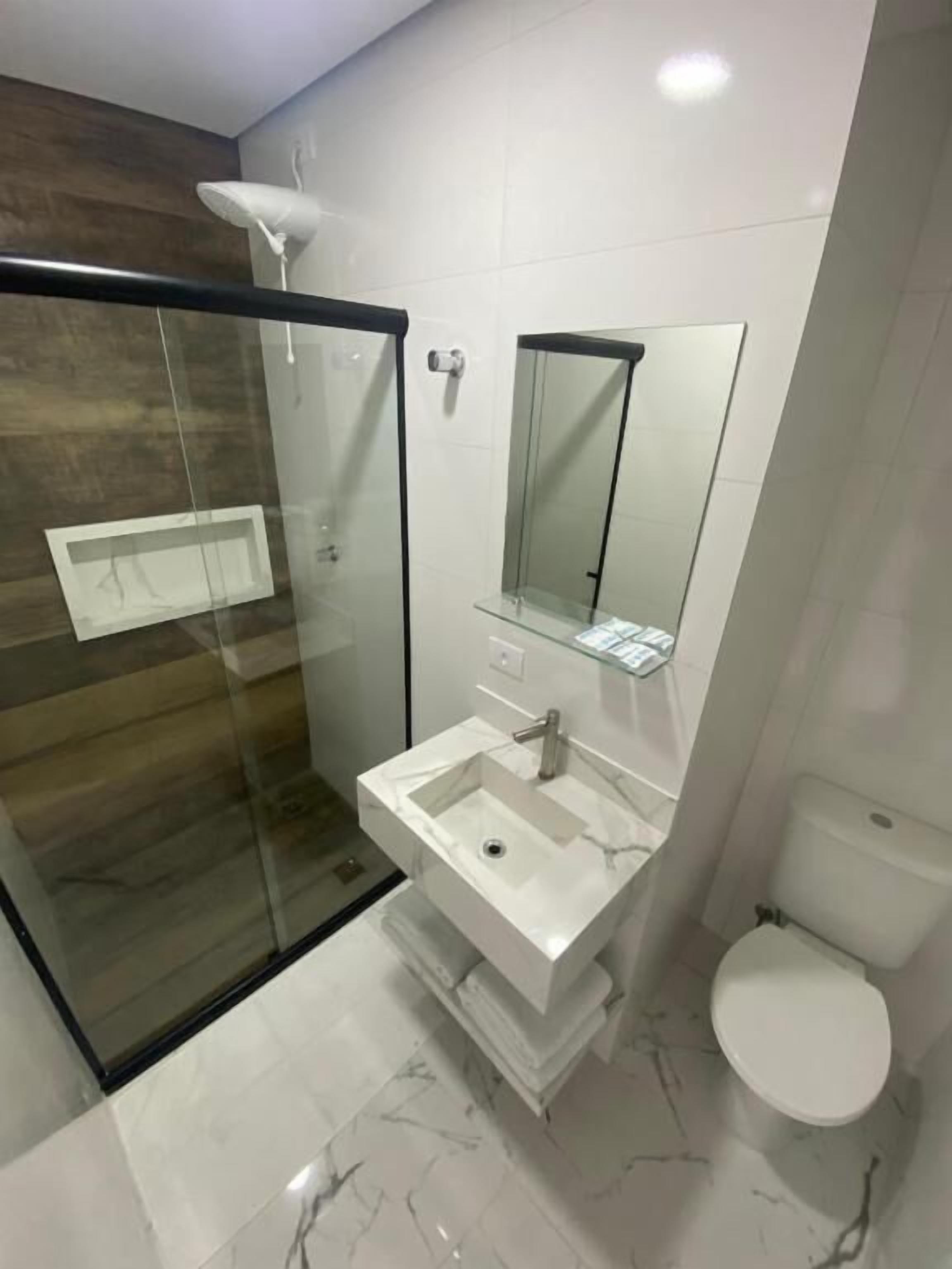 Un baño moderno con cabina de ducha de vidrio, un lavamanos blanco y un inodoro.