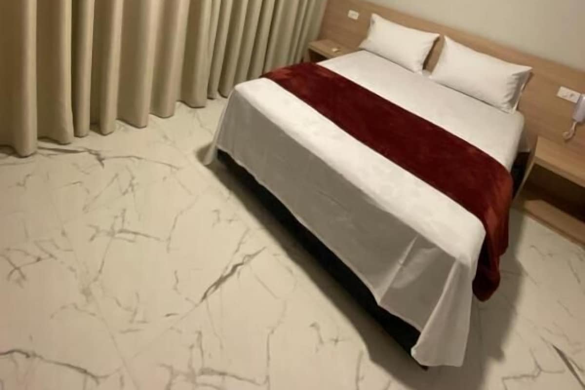 Habitación de hotel con cama, cortinas, mesita de noche y teléfono de pared.