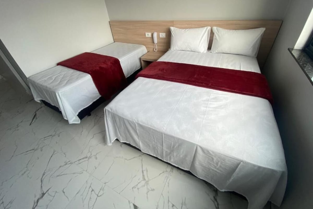 Habitación de hotel con dos camas, cabecera de madera, teléfono y suelo de mármol.