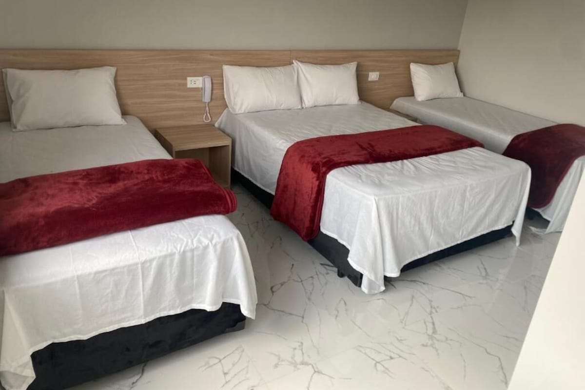 Una habitación de hotel con tres camas, cada una con ropa de cama blanca y almohadones rojos.